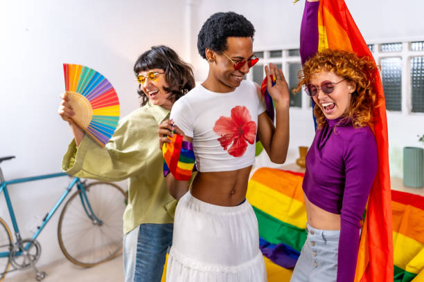 Multi-ethnic and gender diverse friends celebrating pride party at home Happy multi-ethnic and gender diverse friends celebrating pride party at home wearing sunglasses and using hand fan and rainbow flags while dancing gay man men sunglasses party stock pictures, royalty-free photos & images