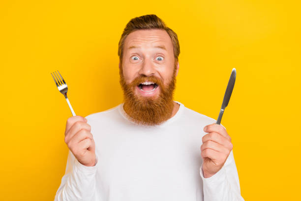istock Photo portrait of nice young guy hold fork knife excited changes nutrition dressed trendy white look isolated on yellow color background 2184893441