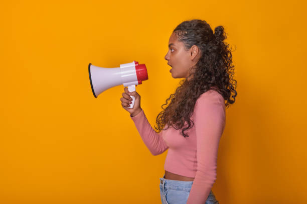 istock A Woman Energetically Speaks Into a Megaphone Against a Vibrant Yellow Backdrop 2184897587