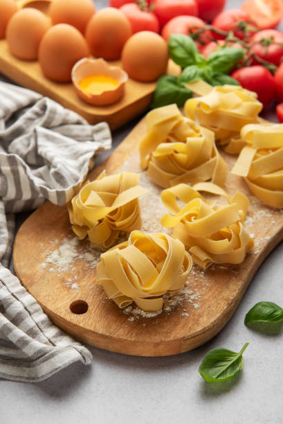 istock Uncooked tagliatelle pasta nests with basil, tomatoes and eggs on wooden cutting board 2184899659