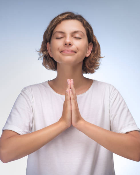 Peaceful Woman with Hands in Prayer Pose and Eyes Closed on Soft Background