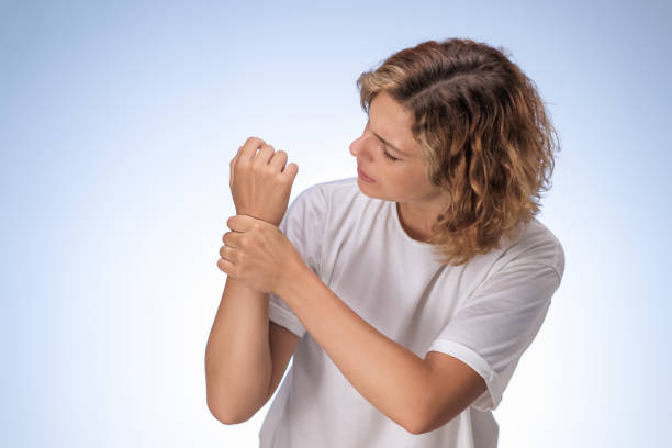 istock Woman Examining Wrist in Pain with Concerned Expression on Light Background 2184905811