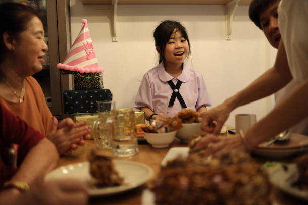 The Asian family gathered for a grnadfather birtday in the dining room, enjoying food together and sharing happy moments.