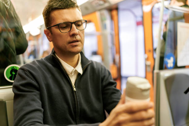 Middle aged male commuter opening water bottle while sitting in subway train on the way from work