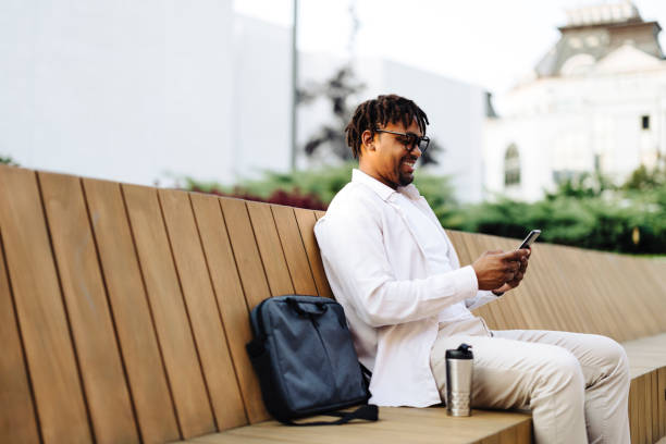 istock Young business man sitting on the bench and using smart phone 2184913675