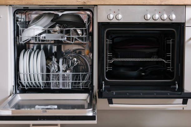 istock Open dishwasher placed beside an oven. Dishwasher loaded with clean dishes. Empty oven 2184915526