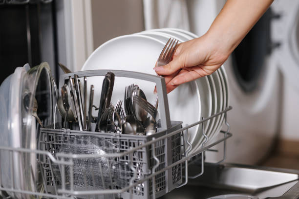 istock Female hand removing clean fork from a loaded dishwasher. Background of open wash machine 2184915880