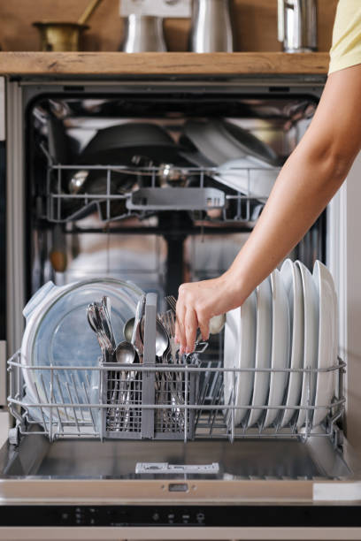 istock Front view from female hand removing clean cutlery from a loaded dishwasher. Background of modern kitchen 2184916082