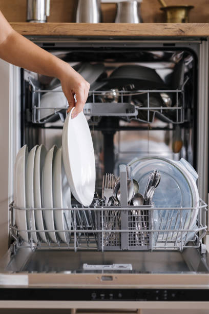 istock Front view from female hand removing clean plate from a loaded dishwasher. Background of modern kitchen 2184916480