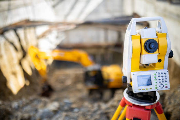 istock Surveying equipment focused in the foreground with an excavator working in a construction site during daylight hours 2184929880