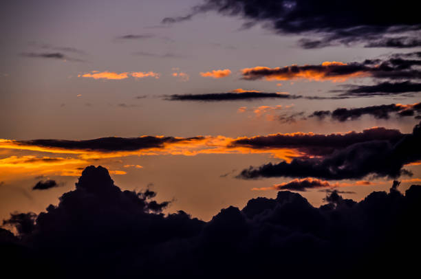 The sky is filled with clouds and the sun is setting. The clouds are dark and the sky is orange