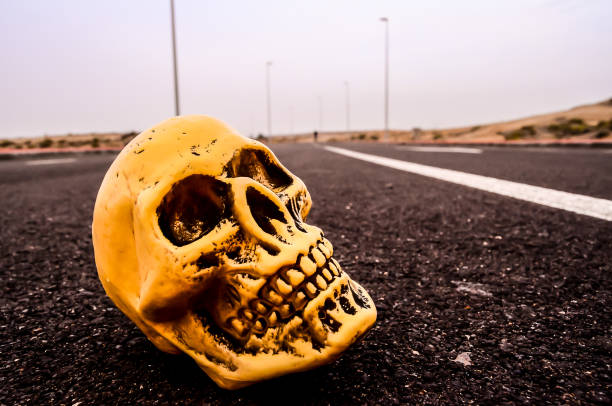 A skull is laying on the road, with a bright yellow color. The skull is positioned in the middle of the road, and it is surrounded by a dark road. The scene gives off a creepy and eerie vibe