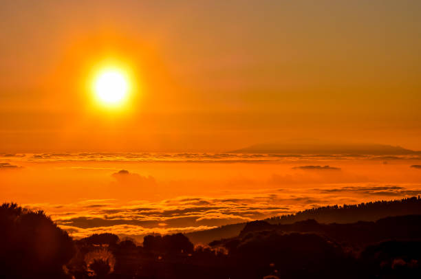 The sun is setting over a mountain range, casting a warm glow over the landscape. The sky is filled with clouds, creating a serene and peaceful atmosphere