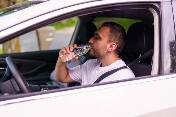 istock Young man driving a white car, drinking cool water from a bottle 2184939597