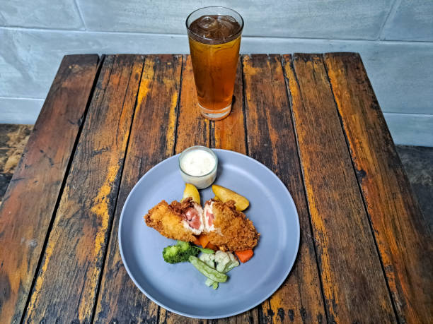 Delicious Chicken Cordon Bleu With Potato Wedges, Snow Peas, Brocolli, Carrot And Mushroom Sauce. Fresh Tea Iced In Glass. Food And Drink Menu.