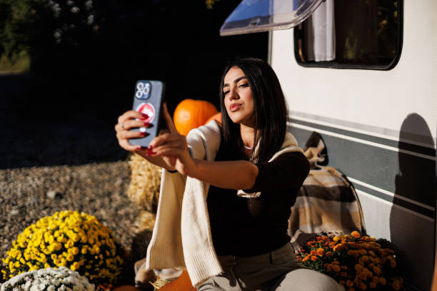 istock Smiling woman taking a selfie while sitting next to a camper van. Capturing adventure and travel moments. 2184957451