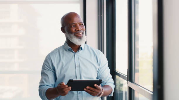 istock Black man, tablet and office window with thinking, idea and digital management with boss and research. Technology, website and mature professional at online consultant agency with business email app 2184958142