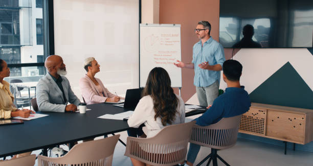 istock Business, man and feedback on whiteboard with people at office for report, presentation and financial growth. Clients, employees and meeting to implement expenses for review, revenue and profit 2184958286