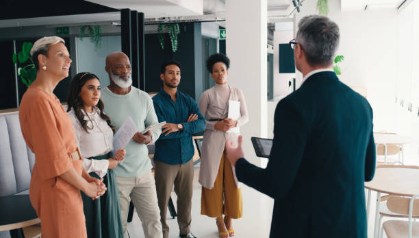istock People, meeting and chat in lobby for business, introduction and office walkthrough with tech. Businessman, new employees and notes in building for advice, learning industry or opportunity discussion 2184958666
