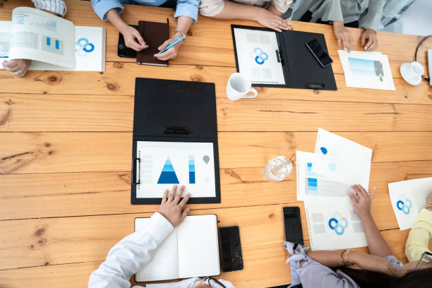 istock Employees Meeting in conference room. There are triangular diagrams, graphs, and related data set aside on a long brown wooden table. 2184960804