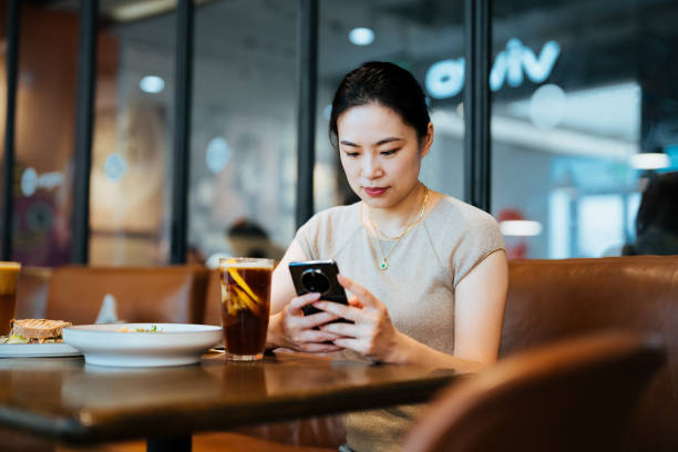 istock Confident young Asian woman using smartphone  while sitting in a cafe having coffee. Enjoying a relaxing moment in the afternoon. Coffee break. Lifestyle and technology. 2184960938