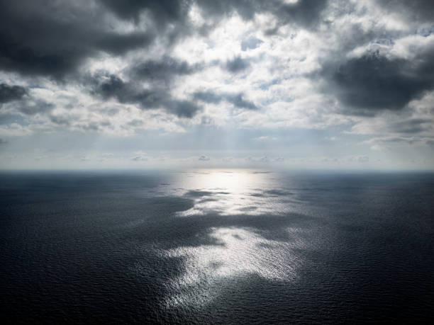 A dramatic seascape with a dark, stormy sky and a single ray of light piercing through the clouds, illuminating the vast ocean below.