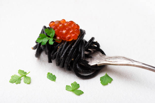 Black pasta with cuttlefish ink and red caviar, served with breadcrumbs fried in olive oil. Volcanic inspiration, seafood paste, black background, minimalist composition. Pasta in the fork, close up