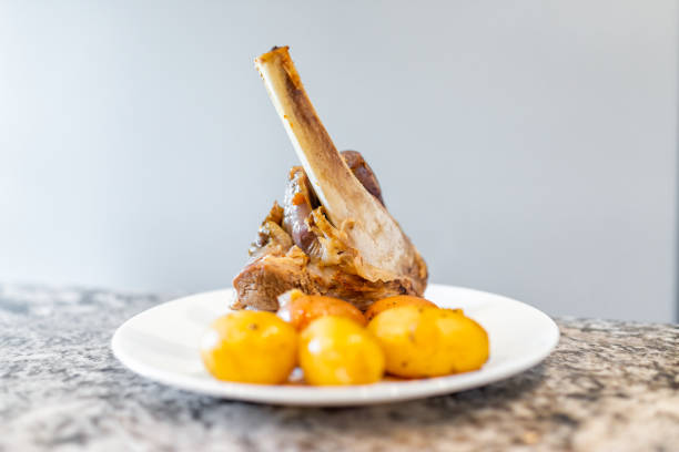 Roasted lamb shanks cooked brown meat stew cooling with potatoes on white plate closeup