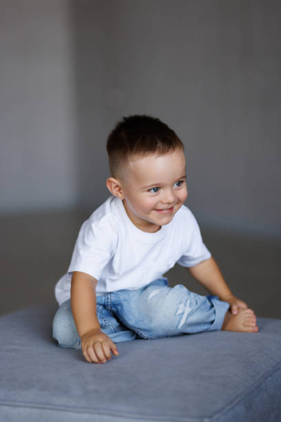 Portrait of an adorable curly-haired baby with big brown eyes, who sits on a white background and looks up with a smile. The concept of stylish clothes for children.