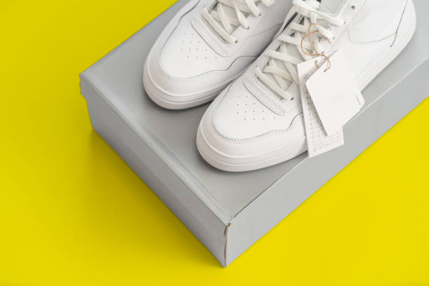 Pair of stylish white sneakers resting on a shoebox against a vivid yellow background, highlighting modern fashion and minimalistic design.