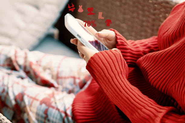 Young Woman in red using mobile Phone App for buying clothes on sale. Sitting cozy on sofa and typing on a phone