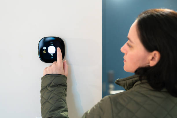 istock woman adjusting temperature on digital thermostat 2185000072