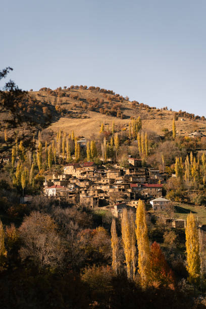 Traditional houses nestled on a hillside, surrounded by colorful autumn foliage, create a picturesque scene