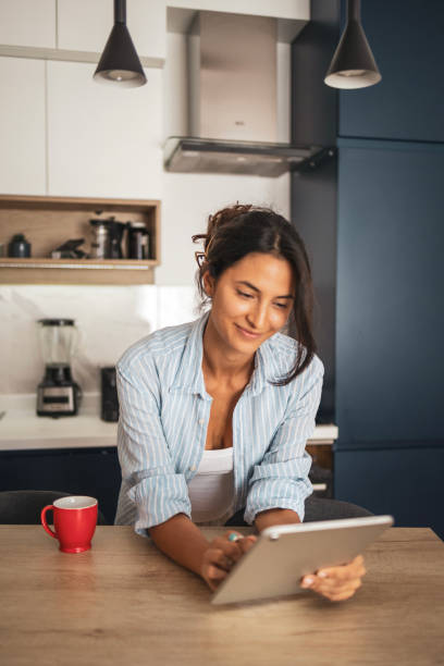 istock Smiling woman standing in the kitchen and using digital tablet 2185005035