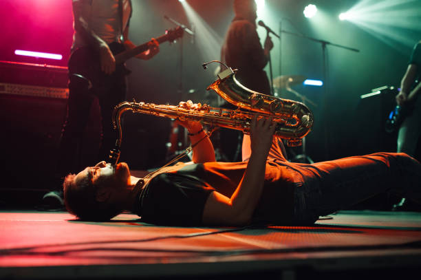 istock Saxophonist lying down playing sax on stage during concert 2185015786