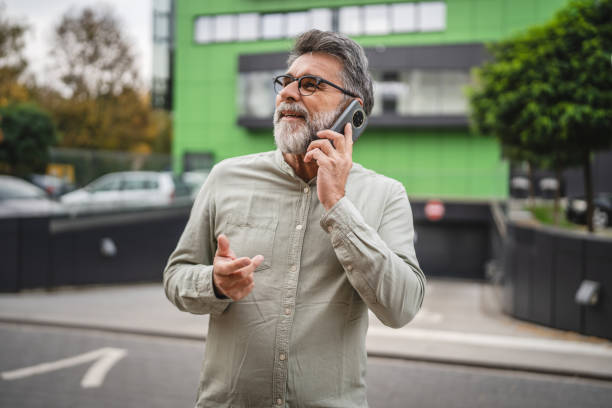 istock senior man talk on mobile phone on break in front green building 2185017211