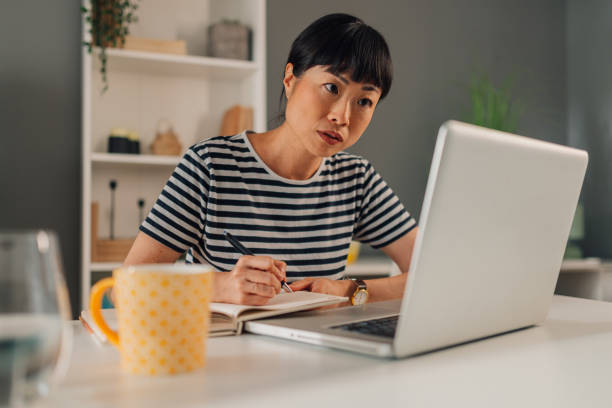 istock Asian woman taking notes while working on her laptop at home. 2185022232