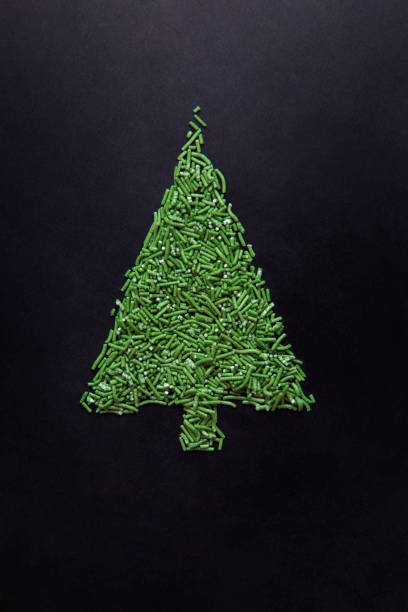 Top view of Christmas tree made of green sugar sprinkles on black fondant.
