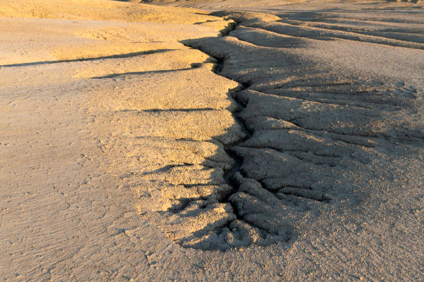 Sunlit view of cracked earth in a mud volcano landscape, showcasing natural erosion and dry textures, highlighting the rugged beauty of an arid environment.