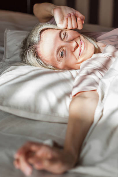 istock Happy middle aged woman sits on bed and stretching arms 2185035096