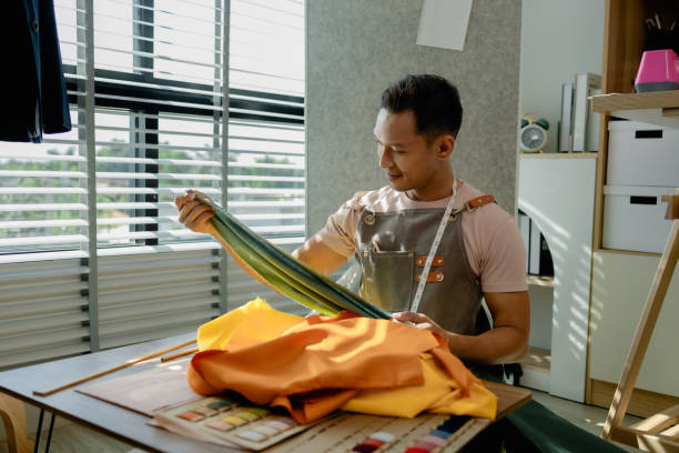istock a fashion designer is working in his studio doing what he loves, he does many things such as using a sewing machine to sew a dress, choosing the fabric to use to make the dress 2185040105