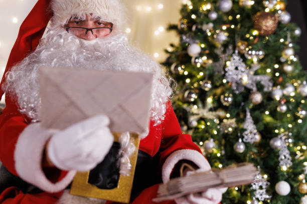 istock Santa sitting by the Christmas tree, reading letters from kids 2185040630