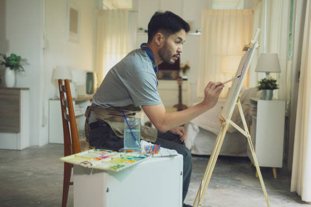 istock Man Painting on Canvas at Easel in Cozy, Well-Lit Home Interior 2185041293
