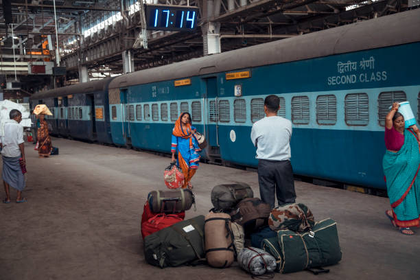 Mumbai, India - Travelers gather at an Indian railway station, with luggage on the ground, as they await their train's departure. The clock shows the time is 17:14, reflecting the busy atmosphere.