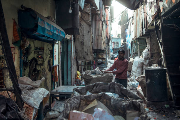 Mumbai, India - A worker navigates through the narrow alleyways of Dharavi Slum, surrounded by waste materials and makeshift structures, illustrating the vibrant yet challenging environment of urban life.