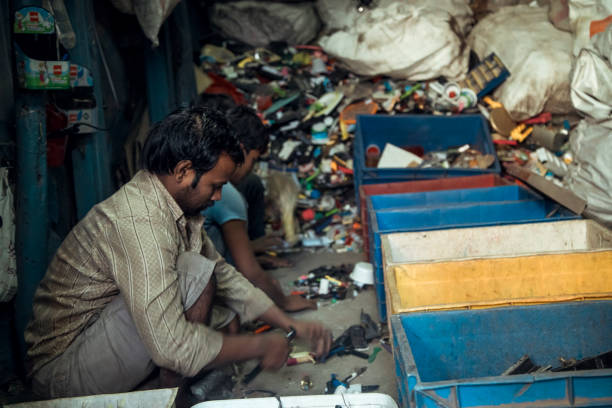 Mumbai, India - In Dharavi Slum, two workers sift through a pile of discarded items, categorizing materials into colorful containers.