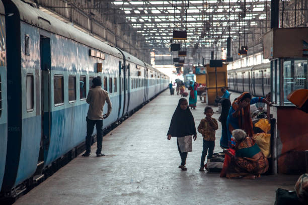 Mumbai, India - Travelers, including families and children, gather on the platform of a bustling railway station in India, eagerly waiting for their train amid the lively atmosphere.