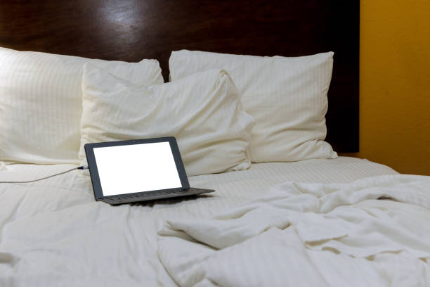 istock Laptop on messy bed with white sheets and scattered pillows in cozy bedroom 2185047370