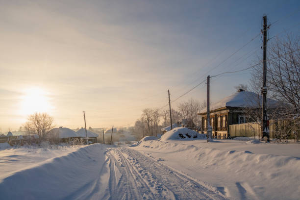 Winter dawn in the village, road through a snow-covered village, severe frost, snow haze. Winter village of Cherdyn. Perm Region, Russia.