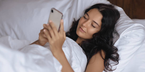 istock Woman Relaxing In Bed Using Smartphone While Wrapped In White Blanket 2185055878